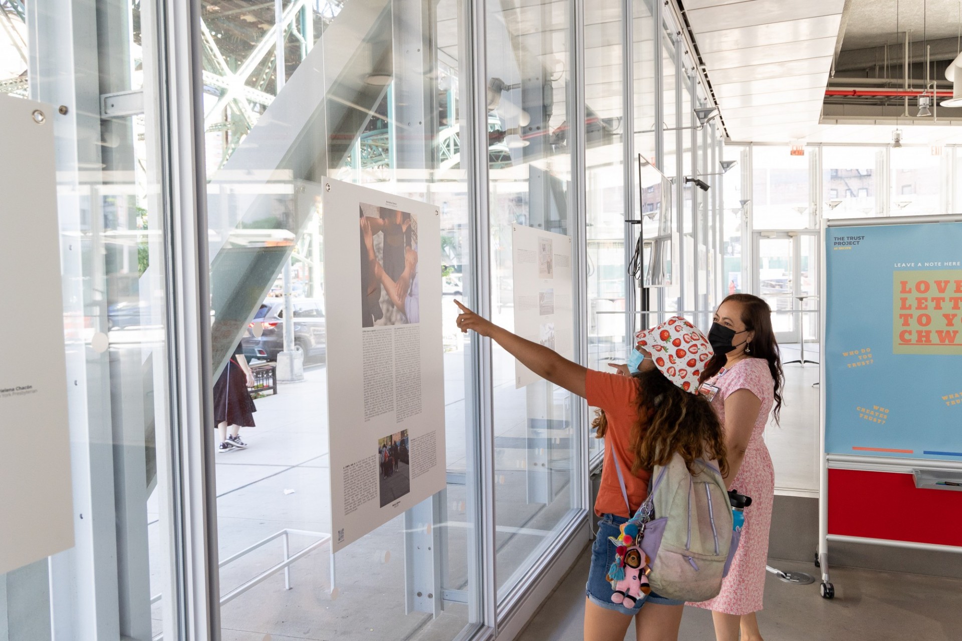 Woman and younger girl standing side by side viewing an image that hangs in the windows of the Forum's Atrium