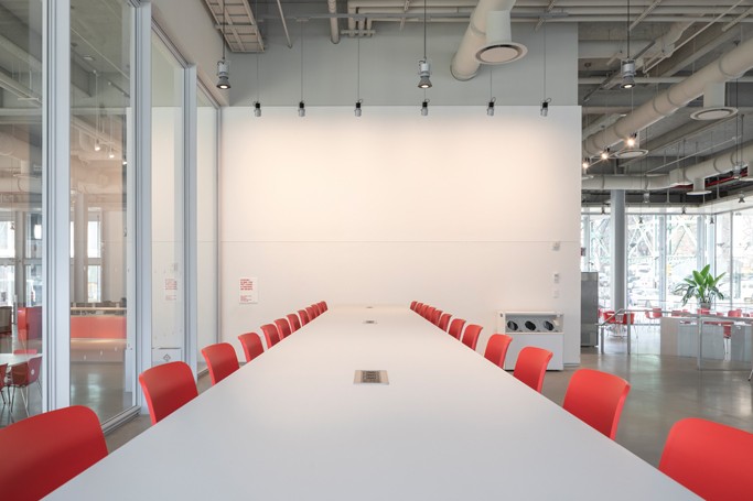 Close-up view of long, thin white high-top conference table with red chairs flanking each side