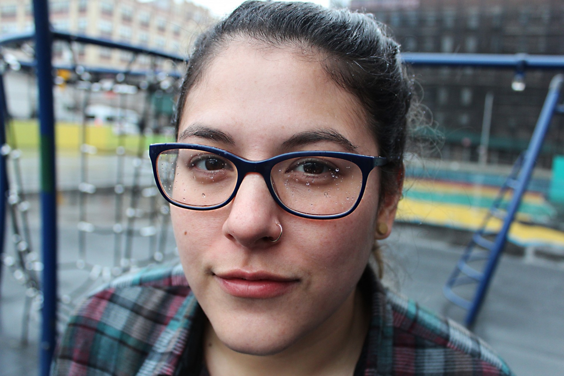 Close-up portrait of a young woman wearing glasses, with a playground in the background