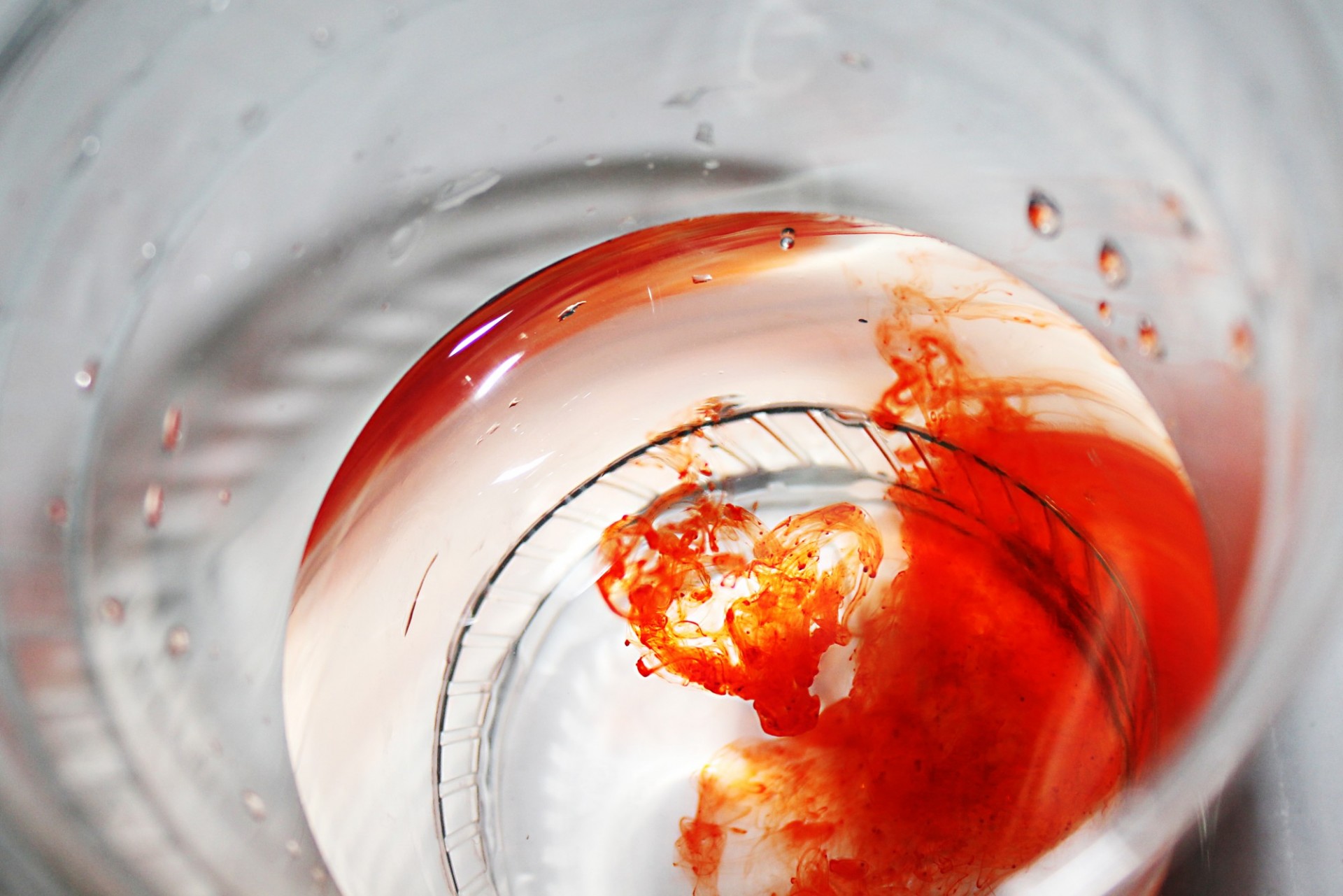 Close-up, bird's eye view into a plastic cup of water with a red dye swirling inside