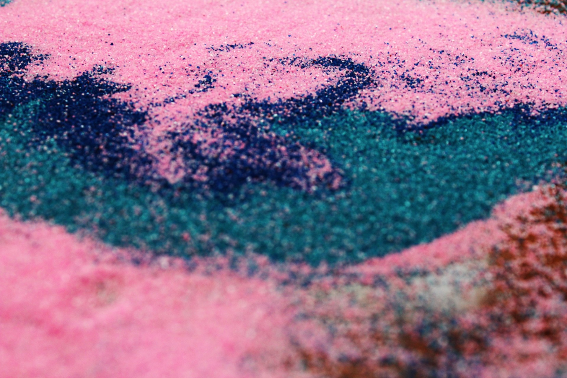 Close-up of small grains of swirling colors including bright pink, dark blue, and teal green