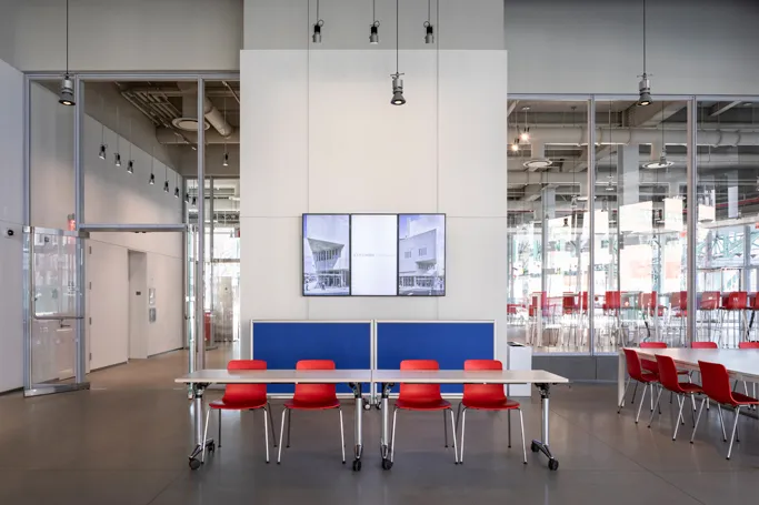 Two registration tables and four chairs set up in The Forum's atrium in front of a three-paneled digital screen