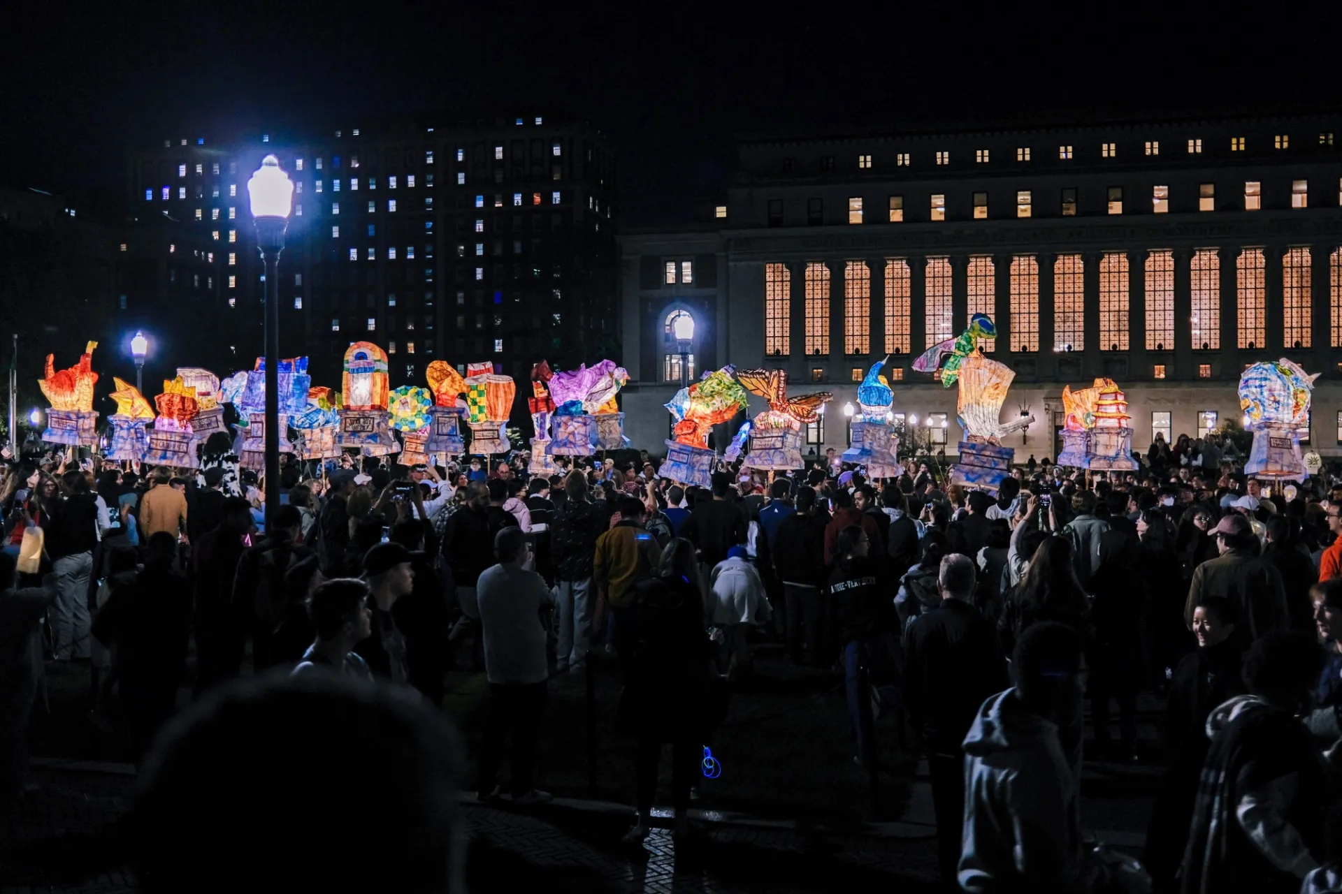 Crowd of people hold colorful lanterns that light up the night sky outside of Low Library