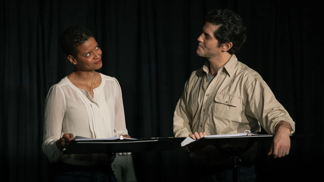 Two actors face each other while reading scripts