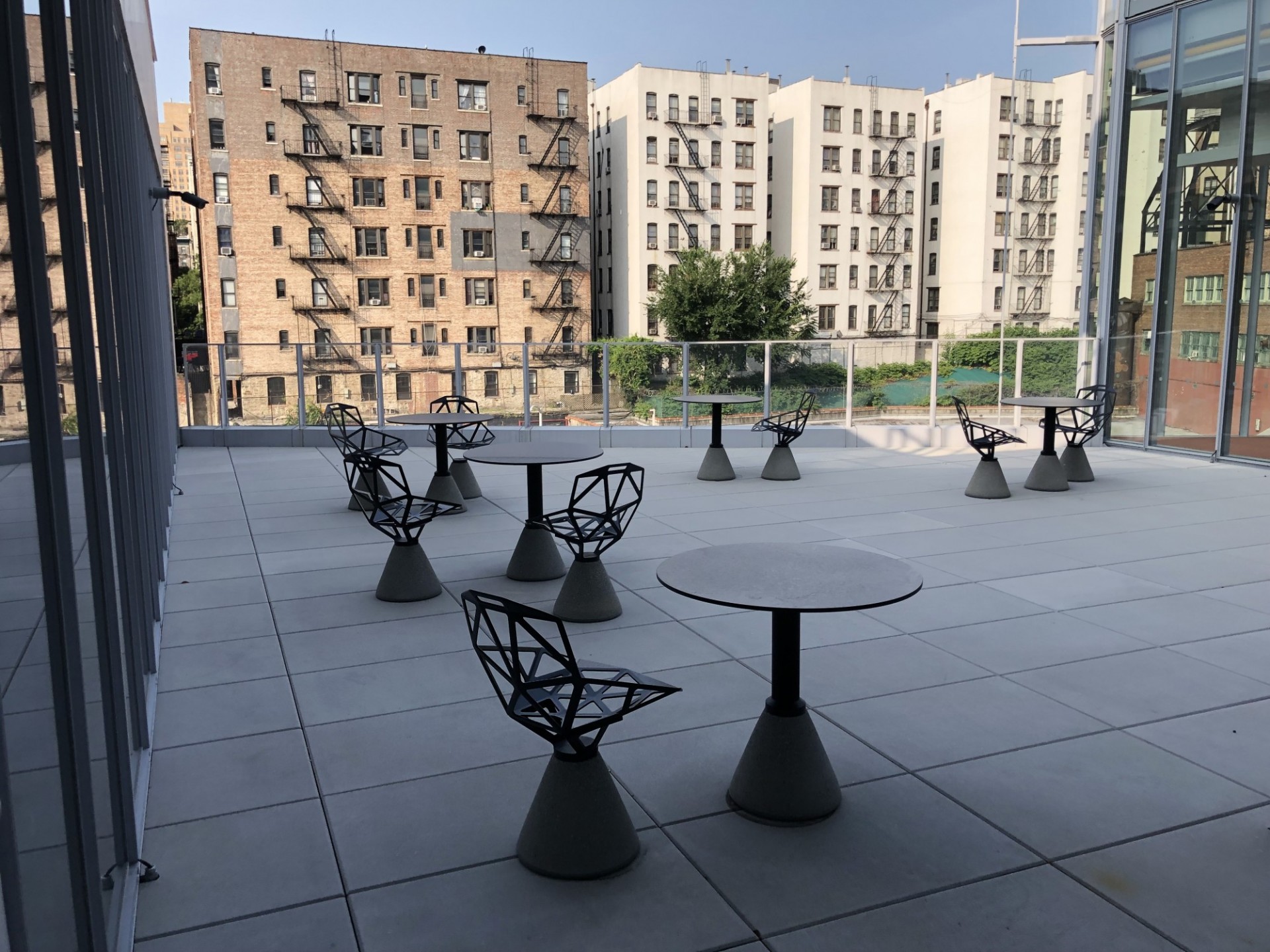 Terrace featuring four round tables with chairs. Neighboring buildings along 125th Street in the background. 